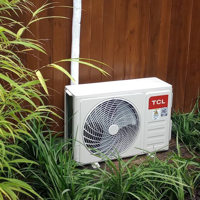 Condensadora TCL em parede de madeira, cercada de plantas